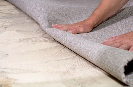 A person's hands laying down carpet padding on a wooden floor